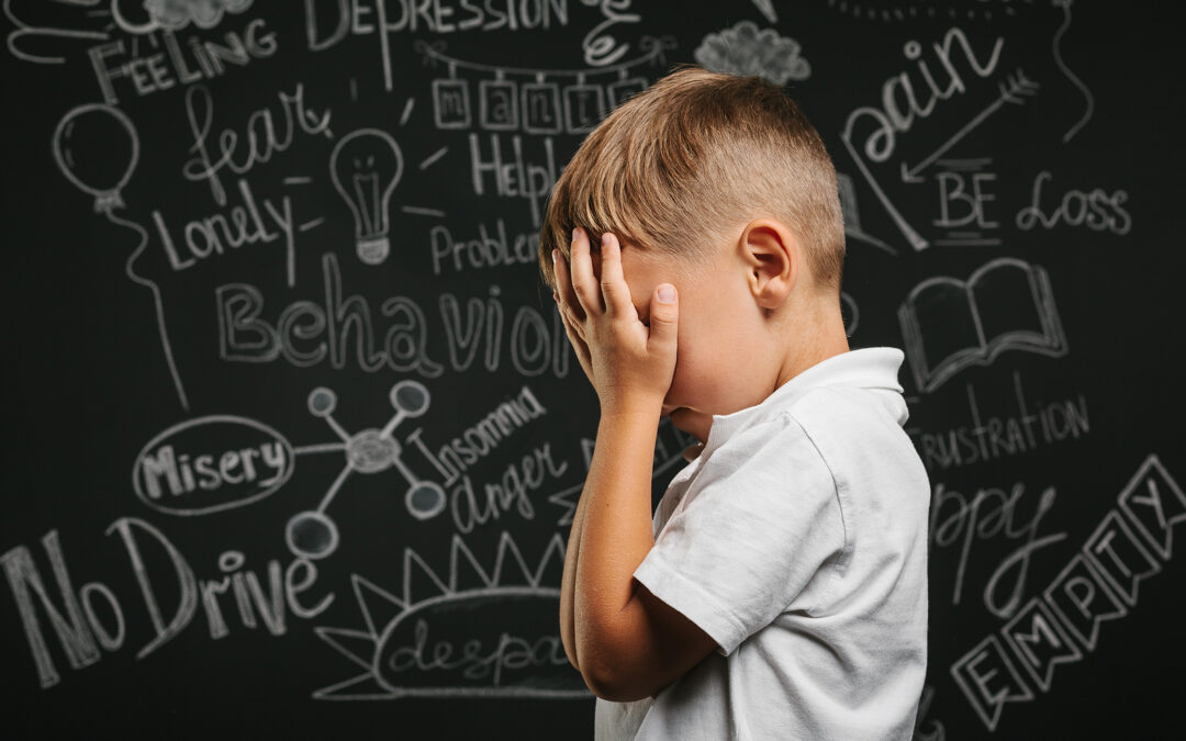 A young boy suffering with dyslexia and anxiety standing by a blackboard with his head in his hands