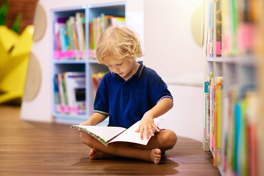 A young boy sitting on the floor reading dyslexia friendly books